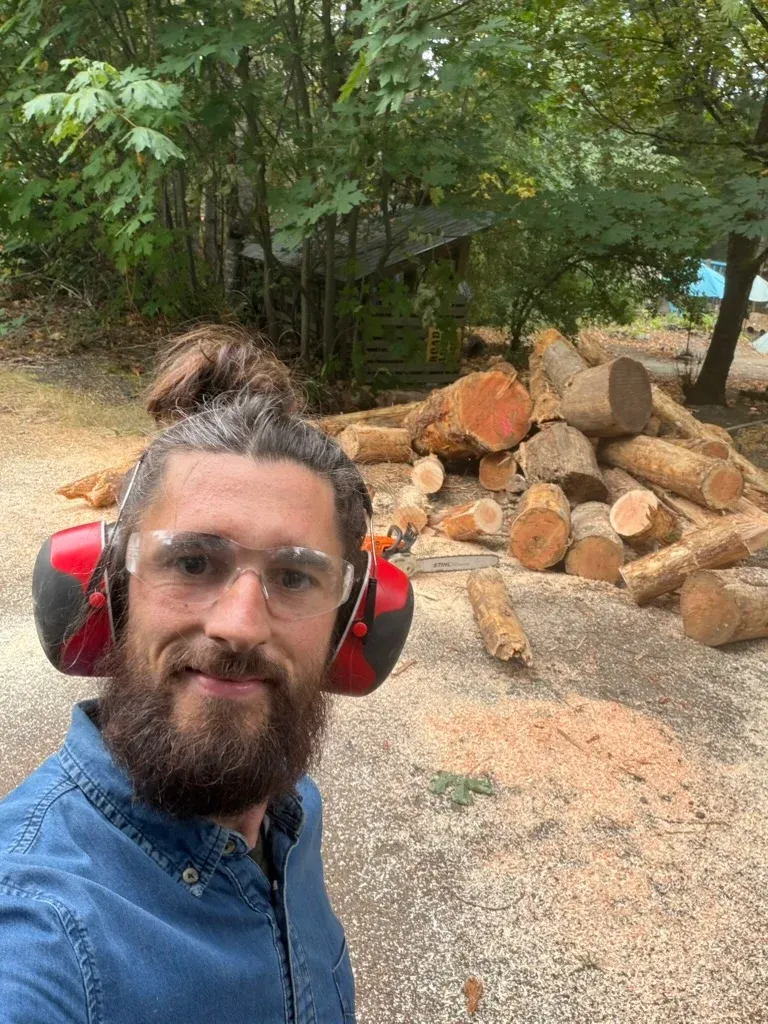Man in ear protection and safety glasses in front of a pile of log rounds, Cowichan Valley BC