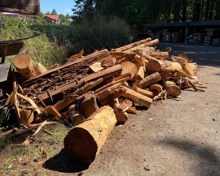 Firewood in Mill Bay BC: a pile of logs and slabs on a gravel driveway