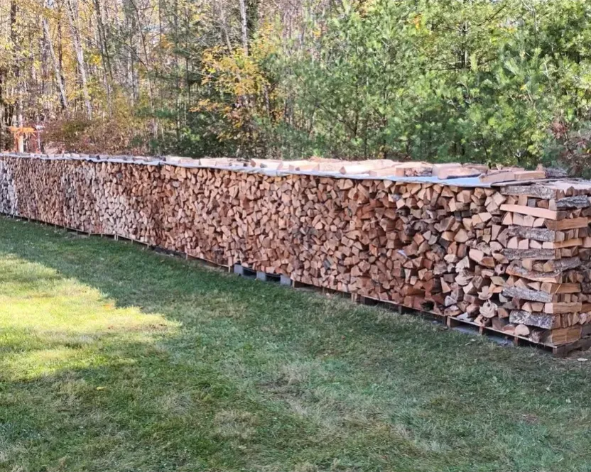 Firewood in North Saanich BC: a long row of split firewood stacked on pallets on a lawn