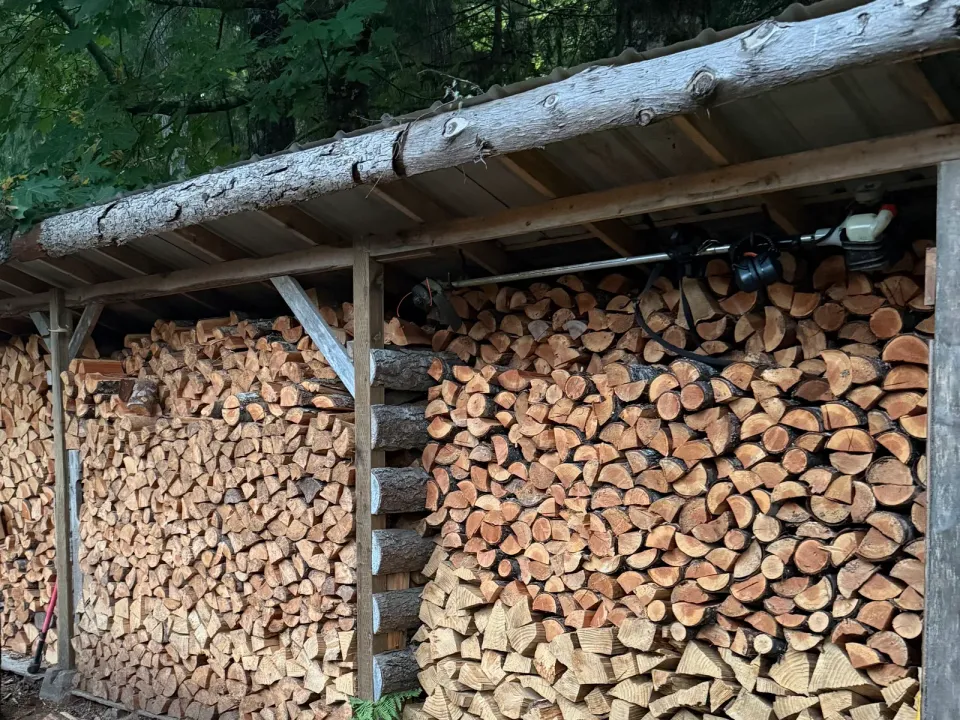 Split firewood stacked in tidy rows under a long open-sided woodshed, Sooke BC