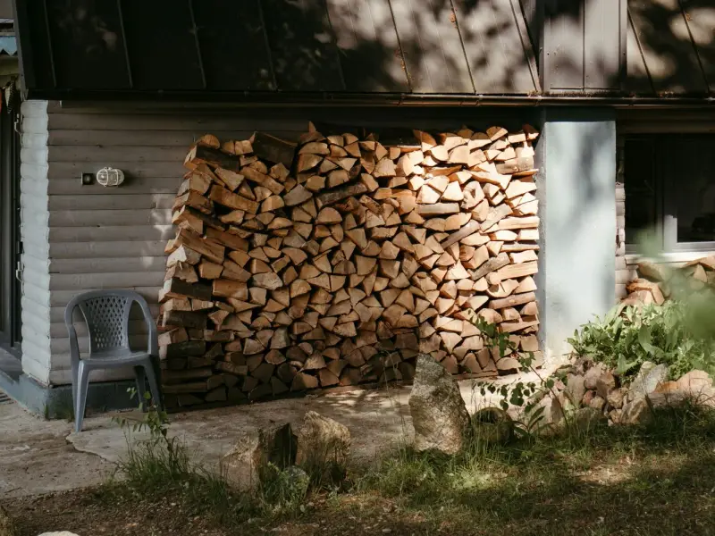 Split firewood stacked against the wall of a grey house, Cowichan Valley BC
